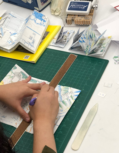 Hands using a ruler and a bone folder to make a fold in a single sheet Risograph zine