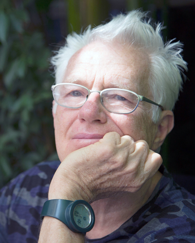 Photo of Harvey Redding, an older man with glasses and white hair. He rests his chin in his left fist and wears a black watch.