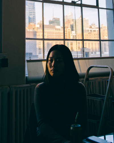 Photograph of Rachel Shim sitting in a dark room against a window. Her face is only partially visible and the rest is in shadow.