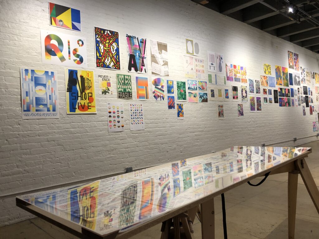 Photograph of Printing the Future Exhibition, riso prints line the walls and zines and books are arranged on wooden tables.