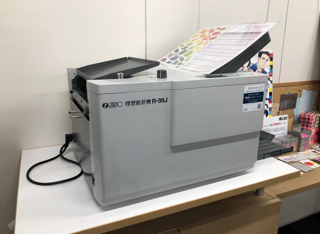 A grey rectangular folding machine on a desk